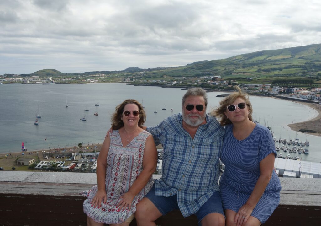 Three family folk sitting on the wall atop the Praia Bay with our house in the distant background

